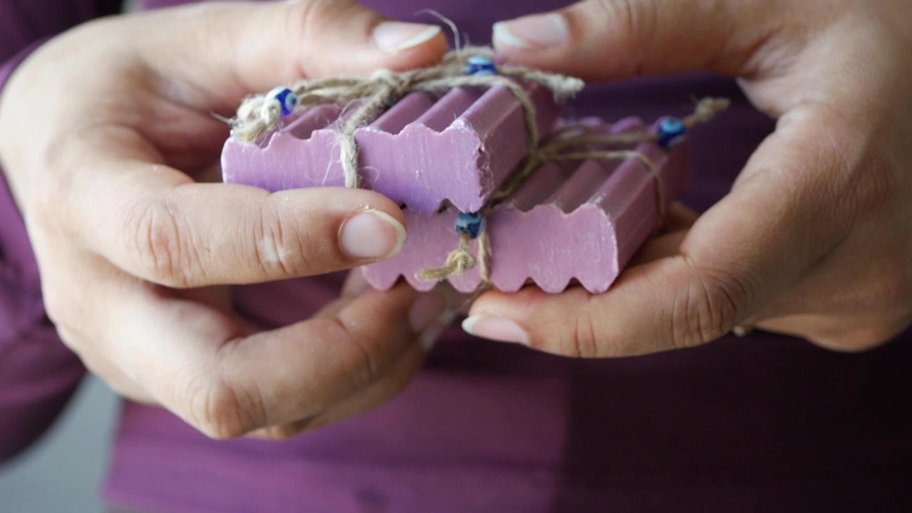Person hält handgemachte lila Seifenstücke, die mit Bindfaden zusammengebunden sind
