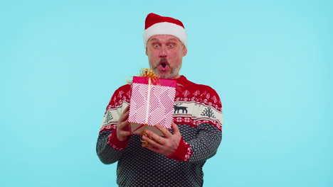 Cheerful-man-in-sweater-Santa-Christmas-hat-getting-present-gift-box,-expressing-amazement-happiness