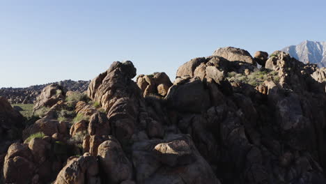 Aerial-view-of-Alabama-Hills-with-rugged-boulders-and-distant-snow-capped-mountains,-capturing-the-vast-landscape-under-a-clear-blue-sky