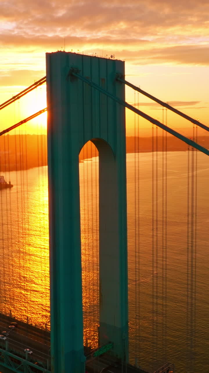 Whitestone bridge in the rays of setting sun. Cars going along the bridge back and forth. Yachts and boats sailing along the East River. Vertical video