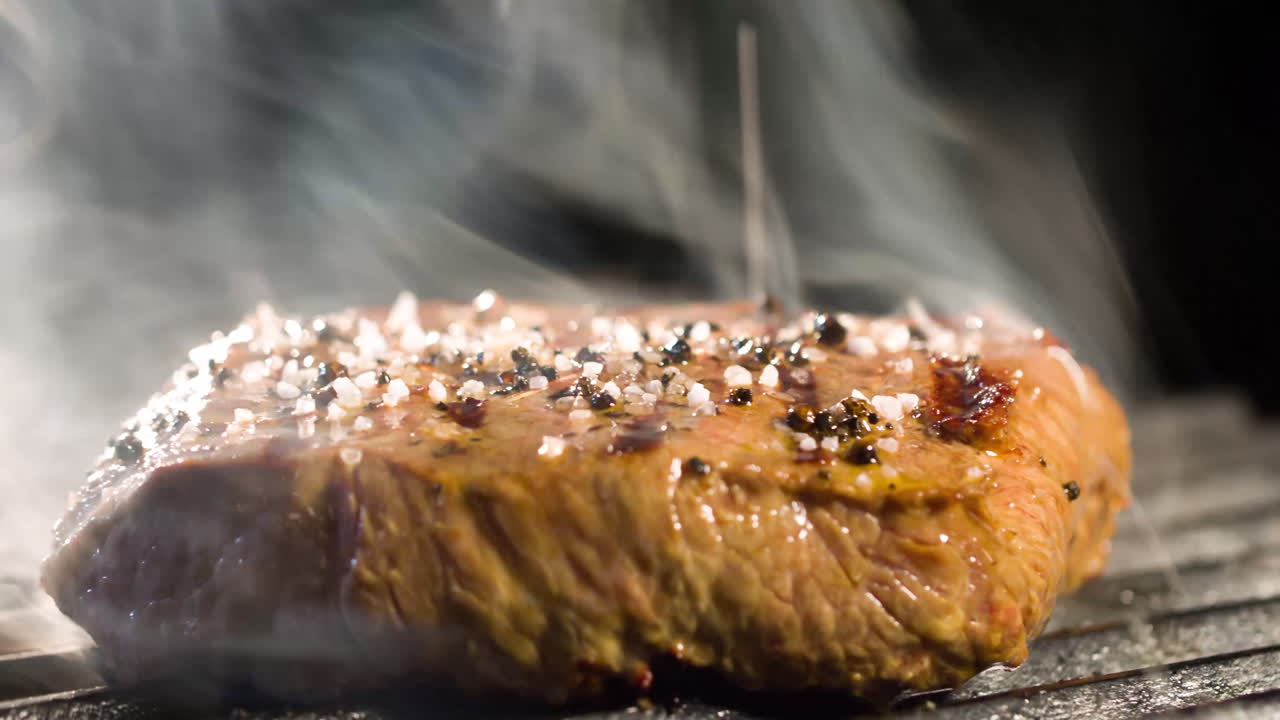 bistec grande a la parrilla, hay humo de las brasas a la carne, vista lateral, primer plano 4k bistec con una vista muy sabrosa 4k