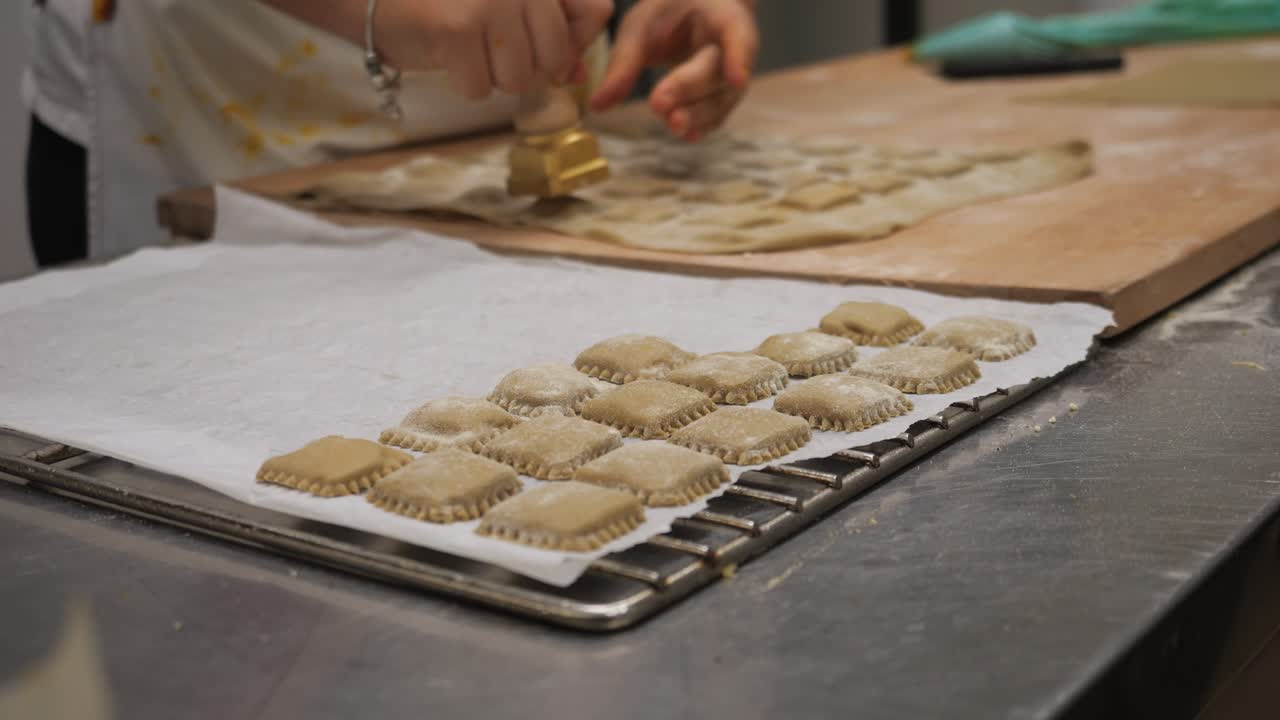 Woman Chef hands preparing fresh pasta, separating tortelli and ravioli parcels from the dough sheet, creating authentic Italian cuisine in a commercial kitchen setting