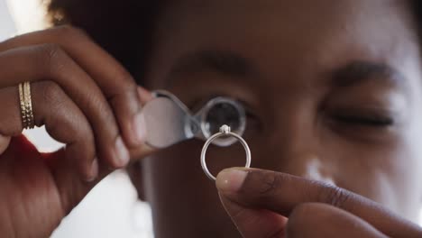 African-american-female-worker-inspecting-ring-with-magnifying-glass-in-workshop-in-slow-motion