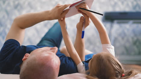 Papá-E-Hija-Hacen-La-Tarea-Juntos-Tirados-En-El-Suelo