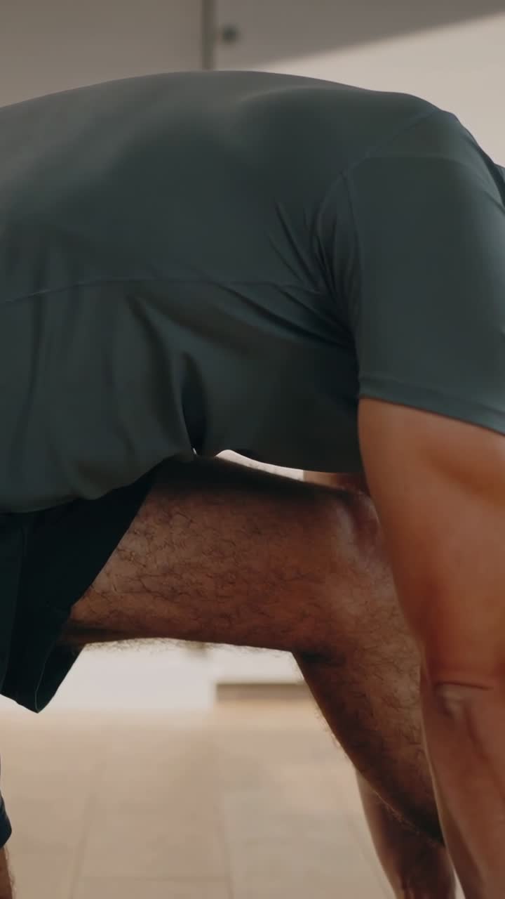 Vertical video: Starting mobility, man moving into lunge stretch at home on wood floor in shorts