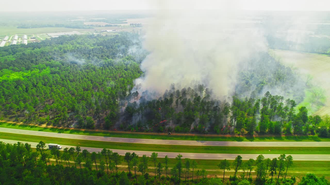 Aerial view of wildfire spreading through dense forest near highway on a hazy day. Georgia, USA