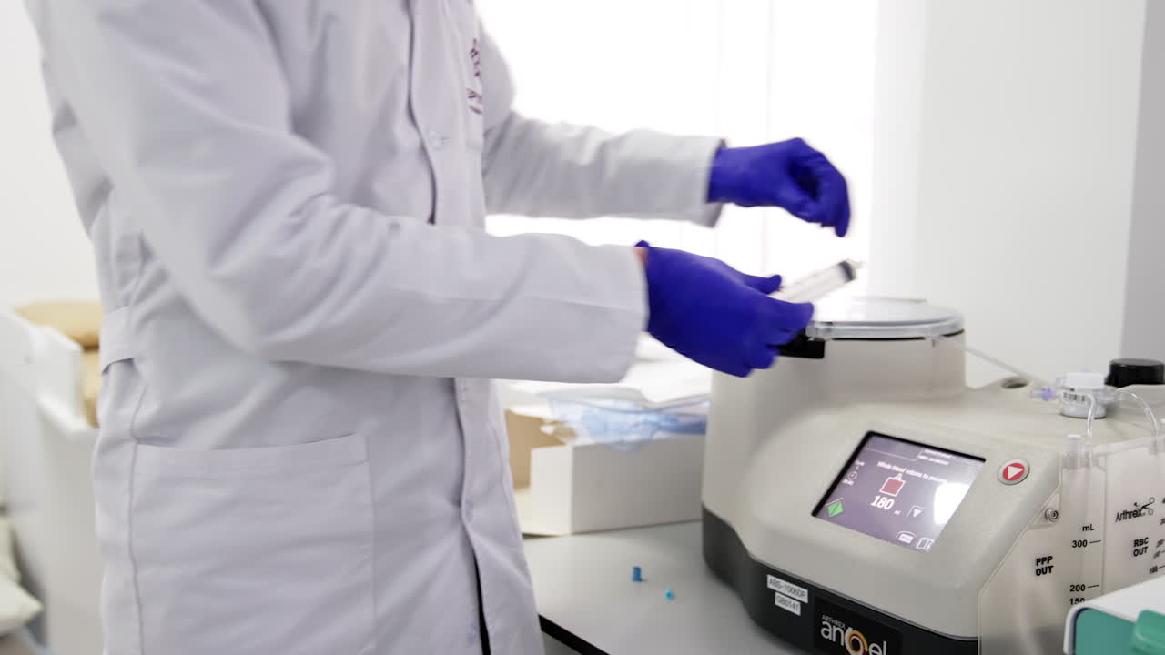 Unrecognized medic in white robe holds a syringe in gloved hands. Doctor attaches a syringe to the centrifuge device.