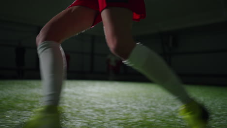 a female soccer player in a red jersey trains indoors on a grass field.