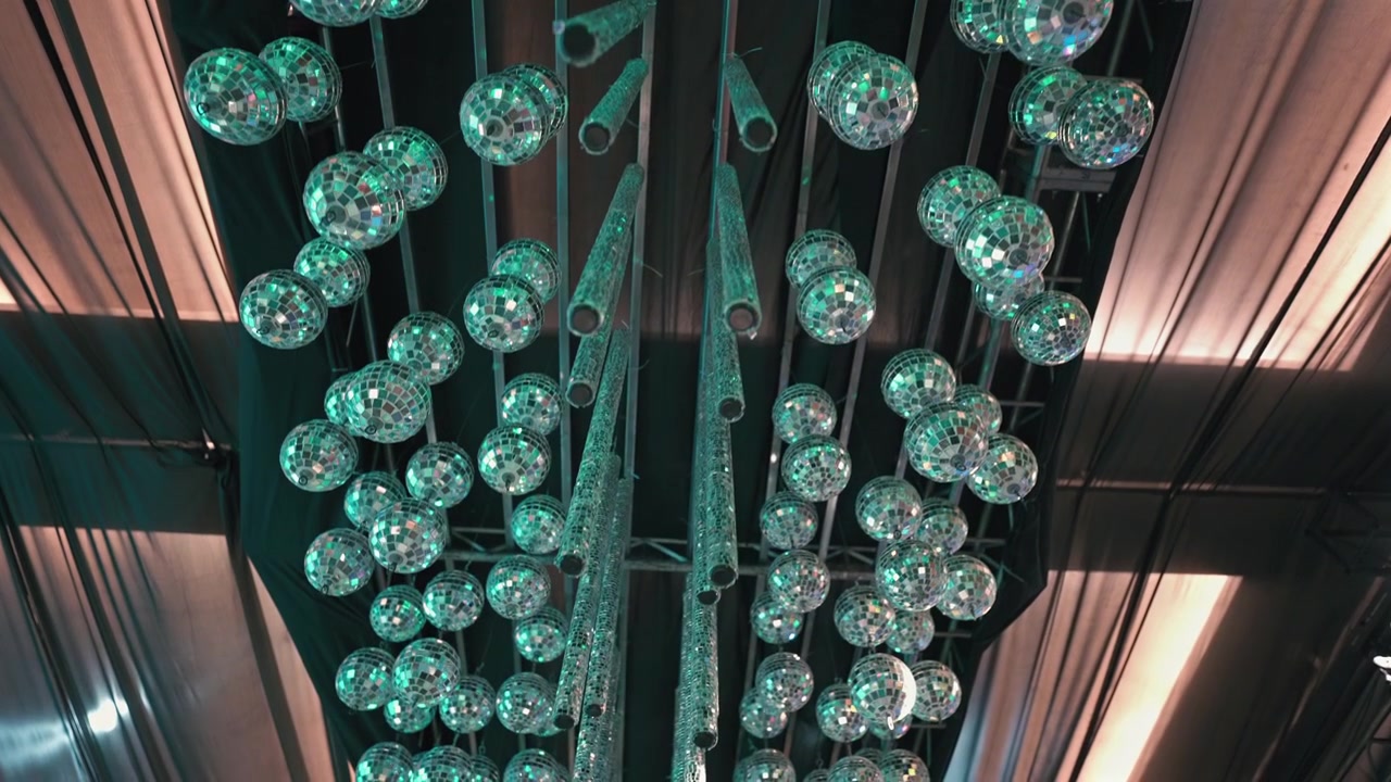 Una dettagliata esposizione di sfere da discoteca appese riflette luci vivaci, creando un'atmosfera dinamica. Ideale per l'ispirazione di design di eventi o per la presentazione di concetti di illuminazione.