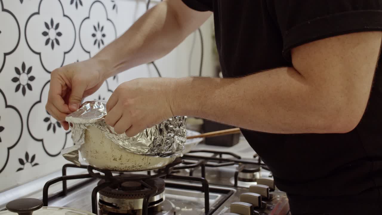 повар накрывает кастрюлю для приготовления пищи фольгой на кухонной плите