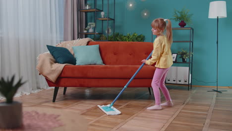 funny toddler girl kid cleaning washes floors with a mop at home dancing, singing in positive mood