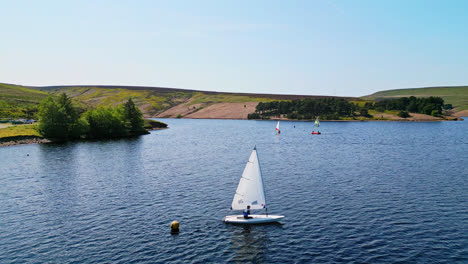 Helles-Sonnenlicht-Beleuchtet-Den-Winscar-Stausee-In-Yorkshire,-Während-Mitglieder-Des-Segelclubs-Mit-Ihren-Booten-Mit-Weißen-Segeln-Auf-Dem-Ruhigen-Blauen-See-An-Einem-Spannenden-Bootsrennen-Teilnehmen