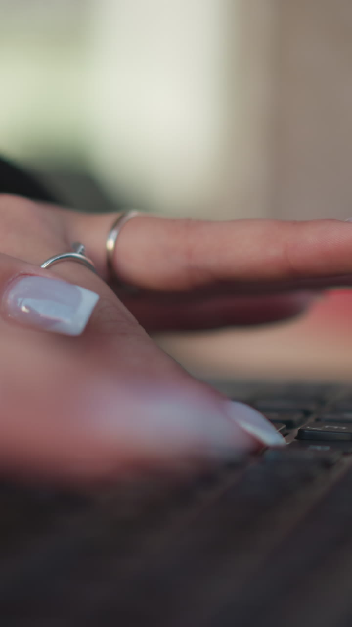 손가락과 손에 초점을 맞추고, 흐릿한 배경으로 노트북 키보드에서 타이핑하는 손의 클로즈업, 은 손과 섬세한 반지로 타이핑하는 행동을 보여줍니다.