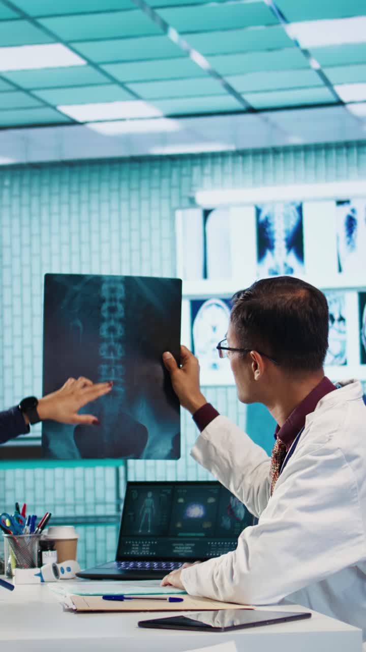 Doctor Examining Spine X-Ray Film and Using Laptop in Medical Office