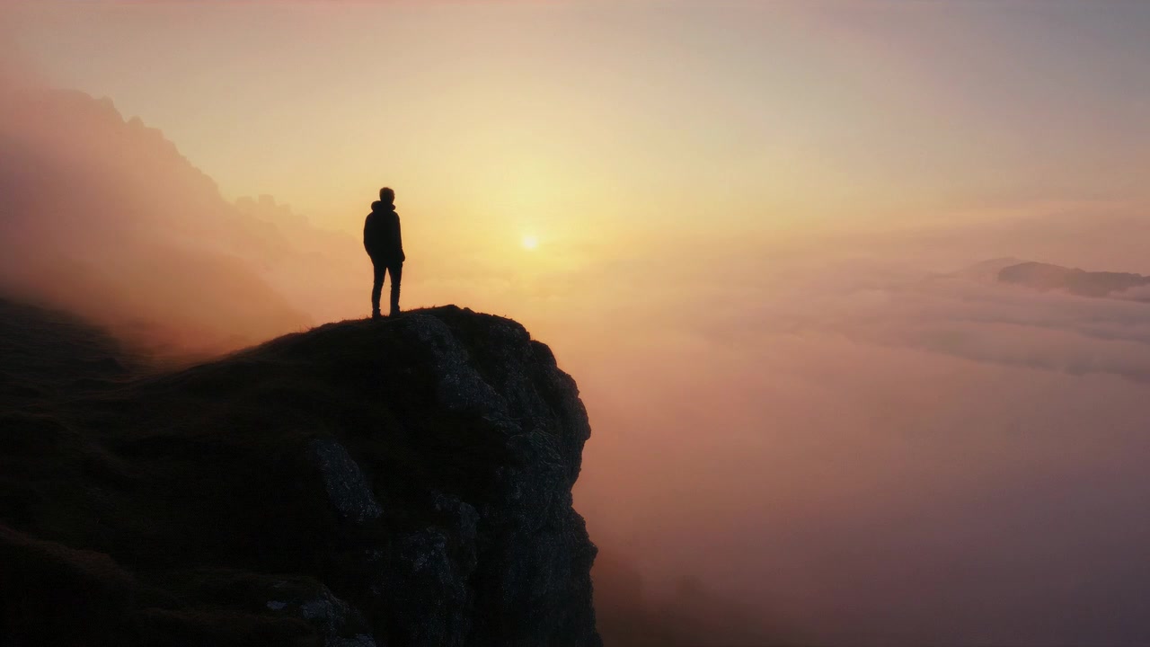 Silhouette of Person on Cliff Edge Watching Time-Lapse Sunset Over Clouds