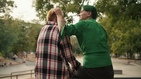 vista trasera de dos chicas lgbt sentadas en una valla en un parque de skate hablando y acariciándose una a la otra. una chica rubia con un corte de pelo corto vk qué llevas puesto una camisa y una chica con cabello verde con un corto corte de pelo en una camisa verde durante su cita lgbt en el parque