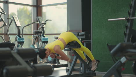 young beautiful hispanic woman performs hyperextension in the gym. the determined woman performs the back extension at the bench in the gym. intense masculine energy. healthy lifestyle. sport concept