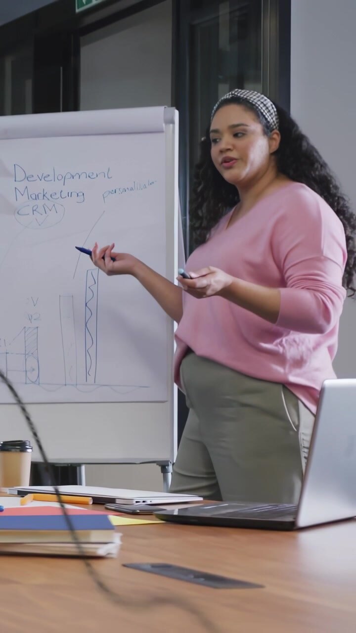 Video verticale: Marketer che disegna una barra blu che mostra un aumento, mentre un'overlay 3D appare sopra un tavolo.