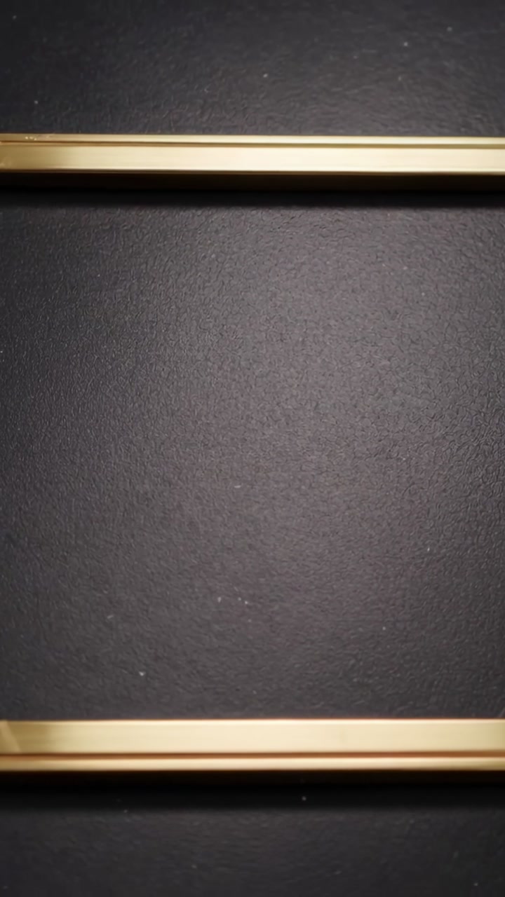 Vertical video: Camera shifting, two gold bars drifting across dark panel with dust specks
