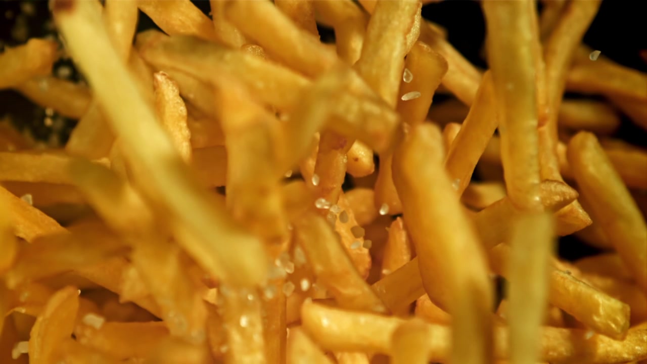 Närbild på gyllene pommes frites som saltas i slow motion
