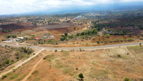 Atemberaubende-Luftaufnahme-Von-Gebäuden-Neben-Einer-Ruhigen-Straße-Mit-Einem-Einzigen-Autofahrer-Im-Ländlichen-Kenia