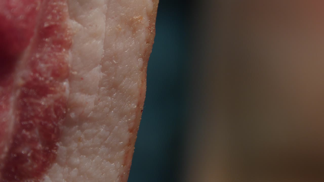 A slice of yummy raw bacon appearing from left. Trucking shot
