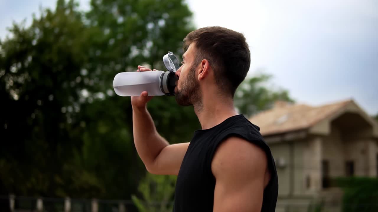 retrato de un hombre deportivo sediento bebiendo agua mineral después de un entrenamiento al aire libre