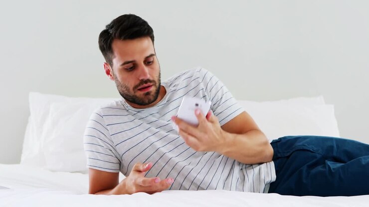 Uomo che utilizza il telefono cellulare sul letto in camera da letto