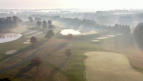 cinematic aerial of sunrise burning off fog above gorgeous country club golf course, autumn leaves