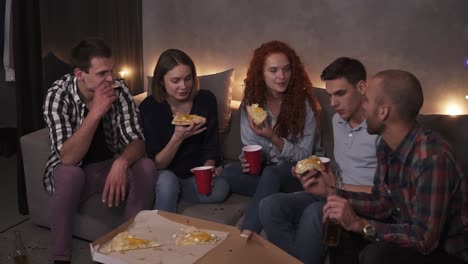 Cheerful-Men-And-Women-Are-Eating-Cheesy-Pizza,-Chatting-Relaxing-During-Indoor-Party-In-Apartment-In-A-Loft-Room