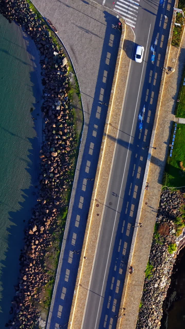 Strada a due corsie con un'auto argentata in movimento, passerelle in pietra e costa rocciosa su entrambi i lati. Vista aerea dall'alto di strada asfaltata su una strada rialzata. Video verticale
