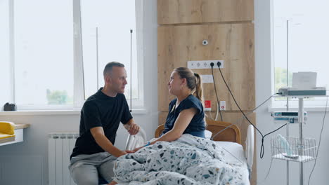 husband and wife expecting a baby are in the ward of maternity hospital. spouses talk and stroking each other.