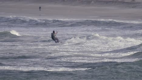 kiteboarding is popular water sport for windy weather, kiteboarder jumping on big waves in peniche, portugal