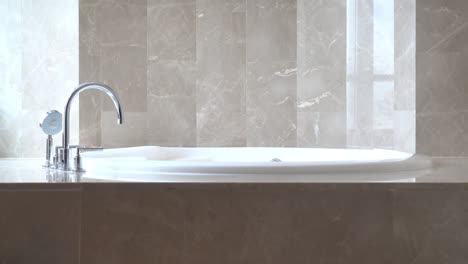 locked shot of stylish modern marble bath sink with natural sunlight from the left, reflecting chrome steel water tap