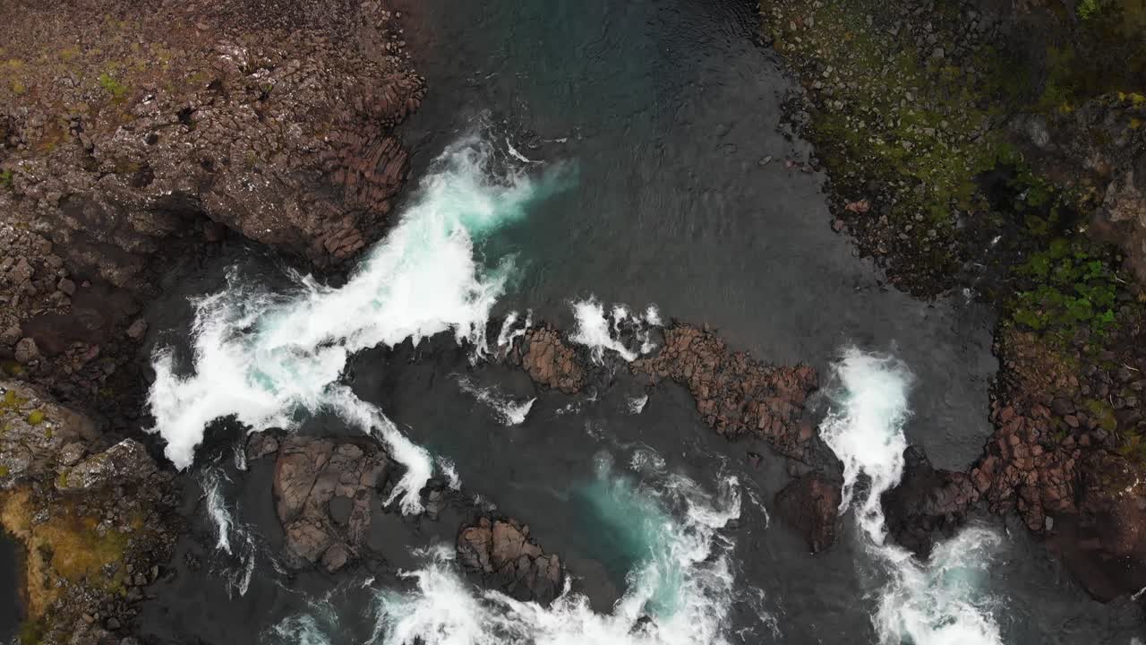 Volando dritto sopra la splendida cascata Glanni in Islanda, vedendo l'acqua turchese che vortica nel fiume, circondata da un paesaggio roccioso e un po' di vegetazione.
