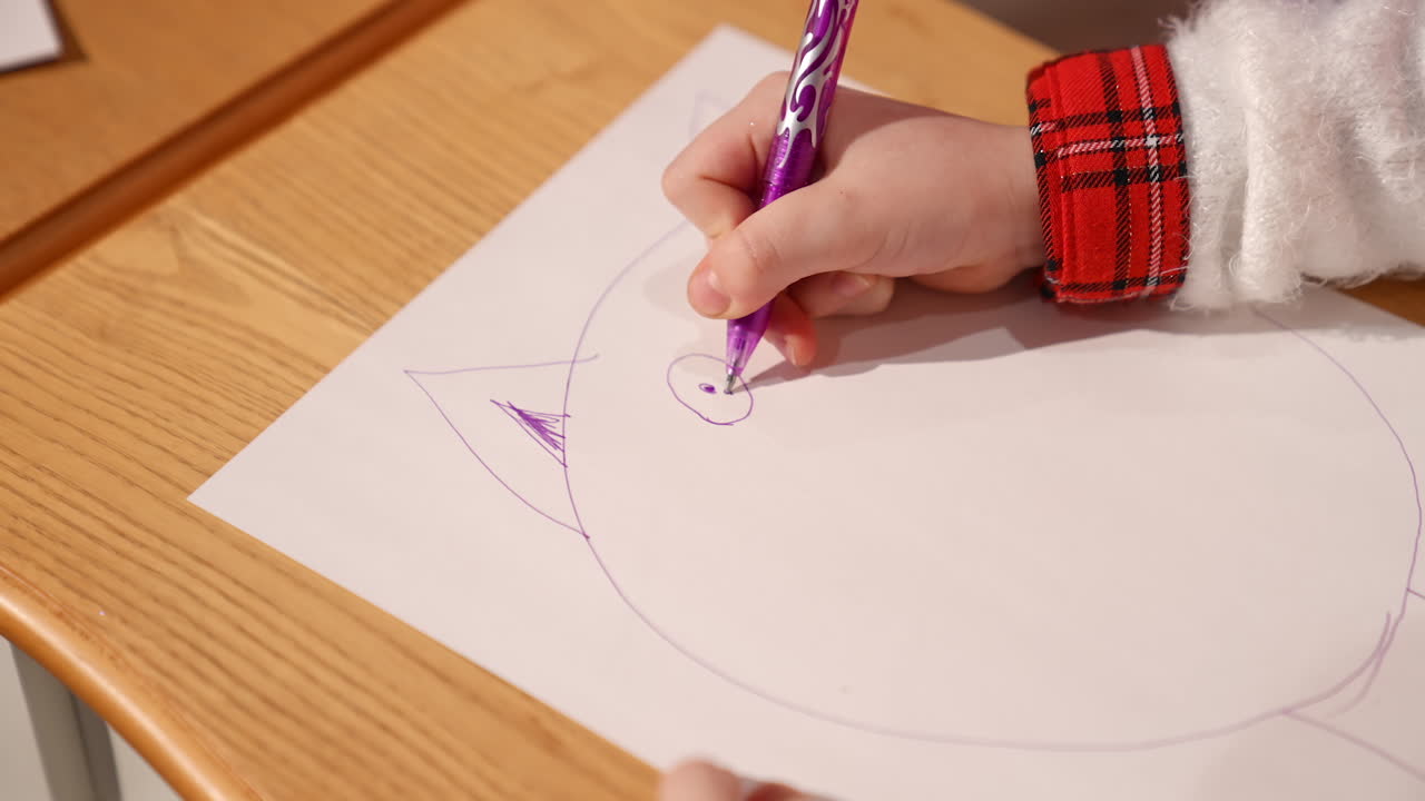 Hand of a little girl paints picture. Paper on the table and a girl's hand drawing with a pen a big animal for Santa. Close-up.