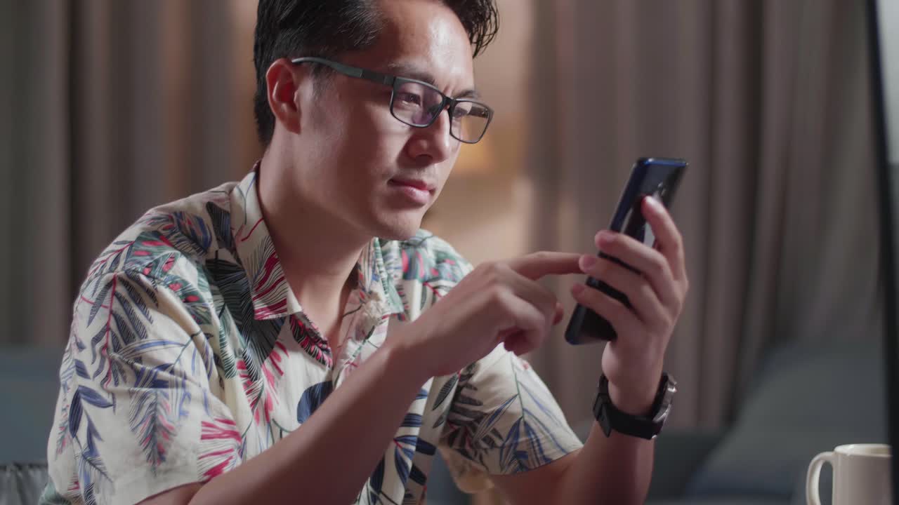 집에서 카메라 에 있는 데스크으로 비디오를 편집하는 동안 스마트폰을 사용하여 체어에 앉은 아시아 남자의 클로즈업