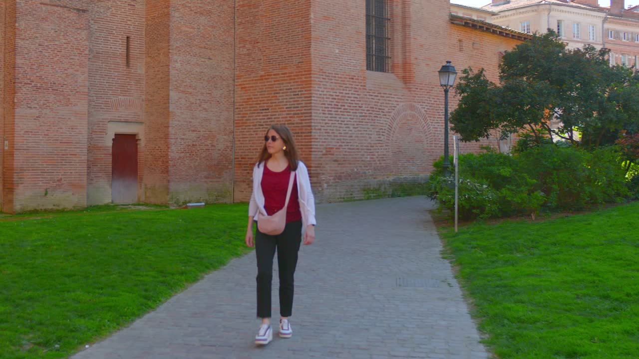 Discover the timeless charm of Toulouse, France, as a woman walks past a historic red-brick church captured from a low angle. Unique architecture characteristic of the "Pink City"