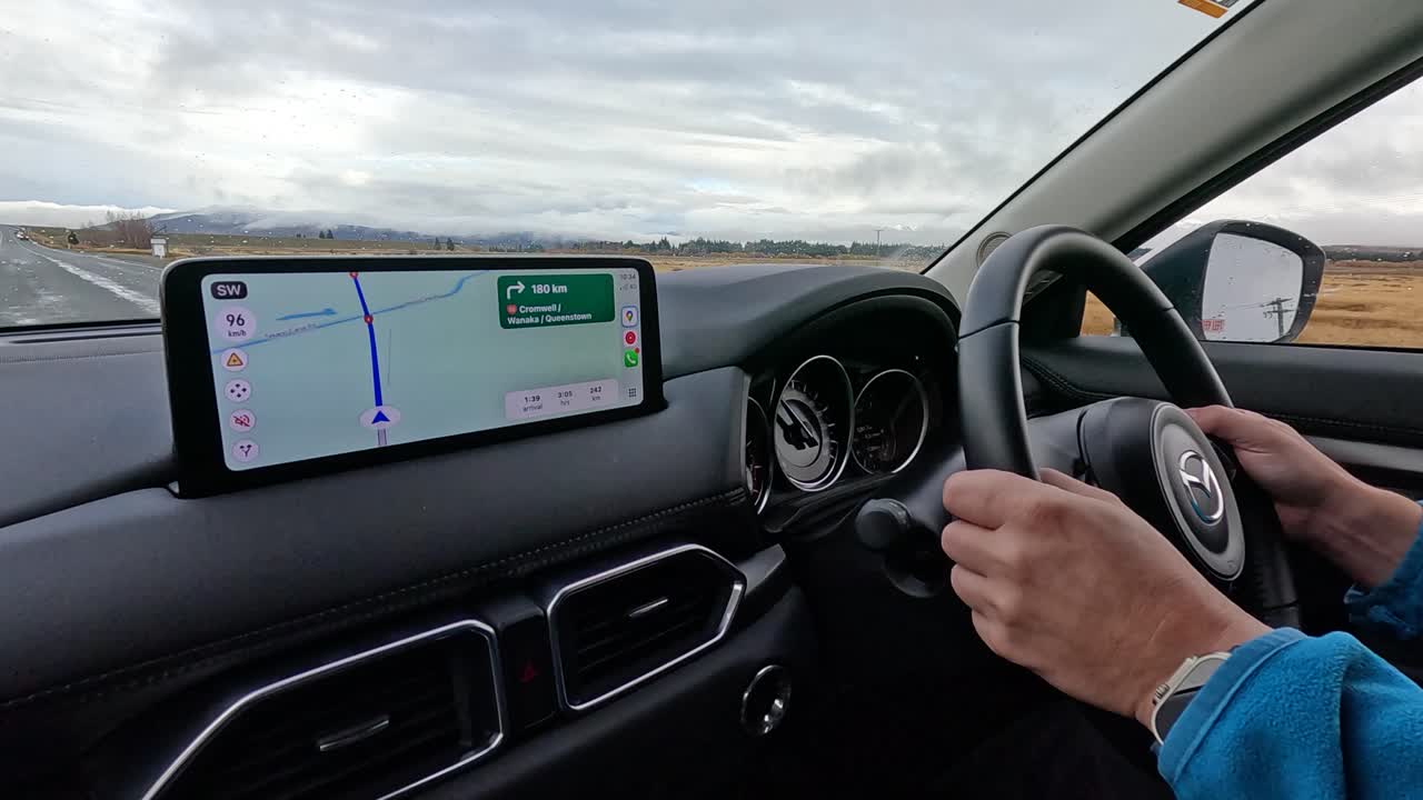 A person drives a modern car along a rural road, following navigation instructions on a dashboard screen. Daylight, steady camera, natural lighting