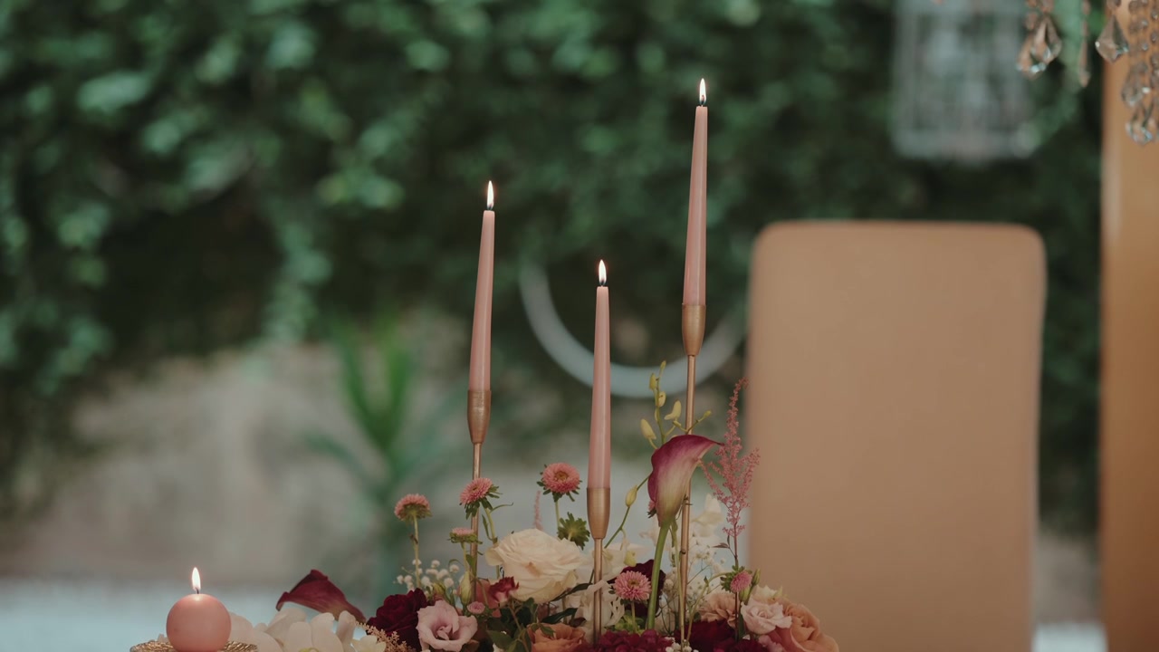 Table centerpiece featuring burning taper and round candles, surrounded by various fresh flowers, creating a warm, romantic atmosphere