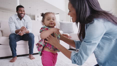 parents at home encouraging baby daughter to take first steps