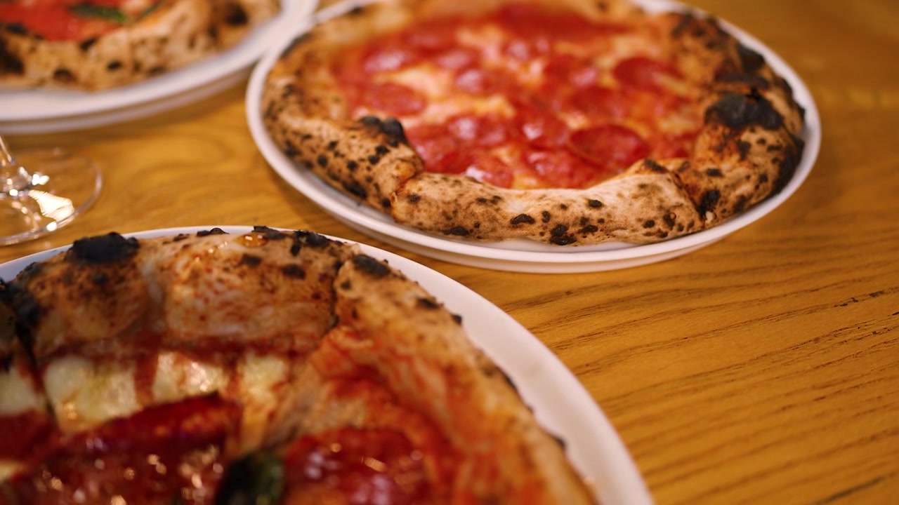 Primo piano in movimento di una pizza calda al salame piccante con mozzarella fusa su un tavolo di legno.