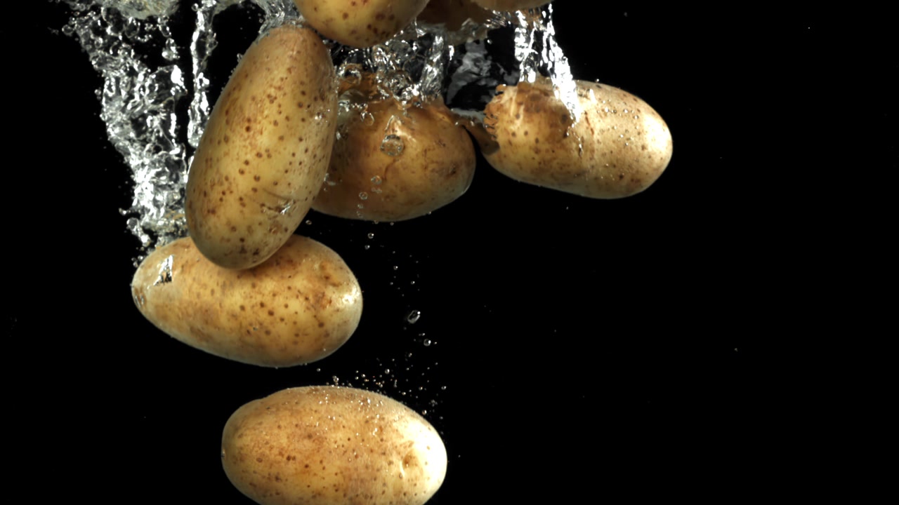 Patate fresche che cadono in acqua con bolle al rallentatore