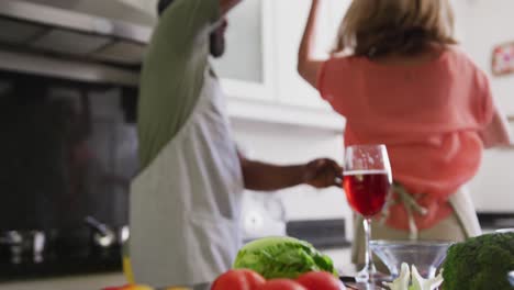 Vielfältiges-älteres-Paar-Mit-Schürzen,-Das-Beim-Zubereiten-Von-Speisen-In-Der-Küche-Tanzt