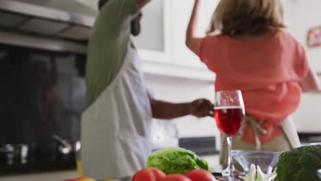 Diversa-Pareja-De-Ancianos-Usando-Delantales-Bailando-Mientras-Preparan-Comida-En-La-Cocina.