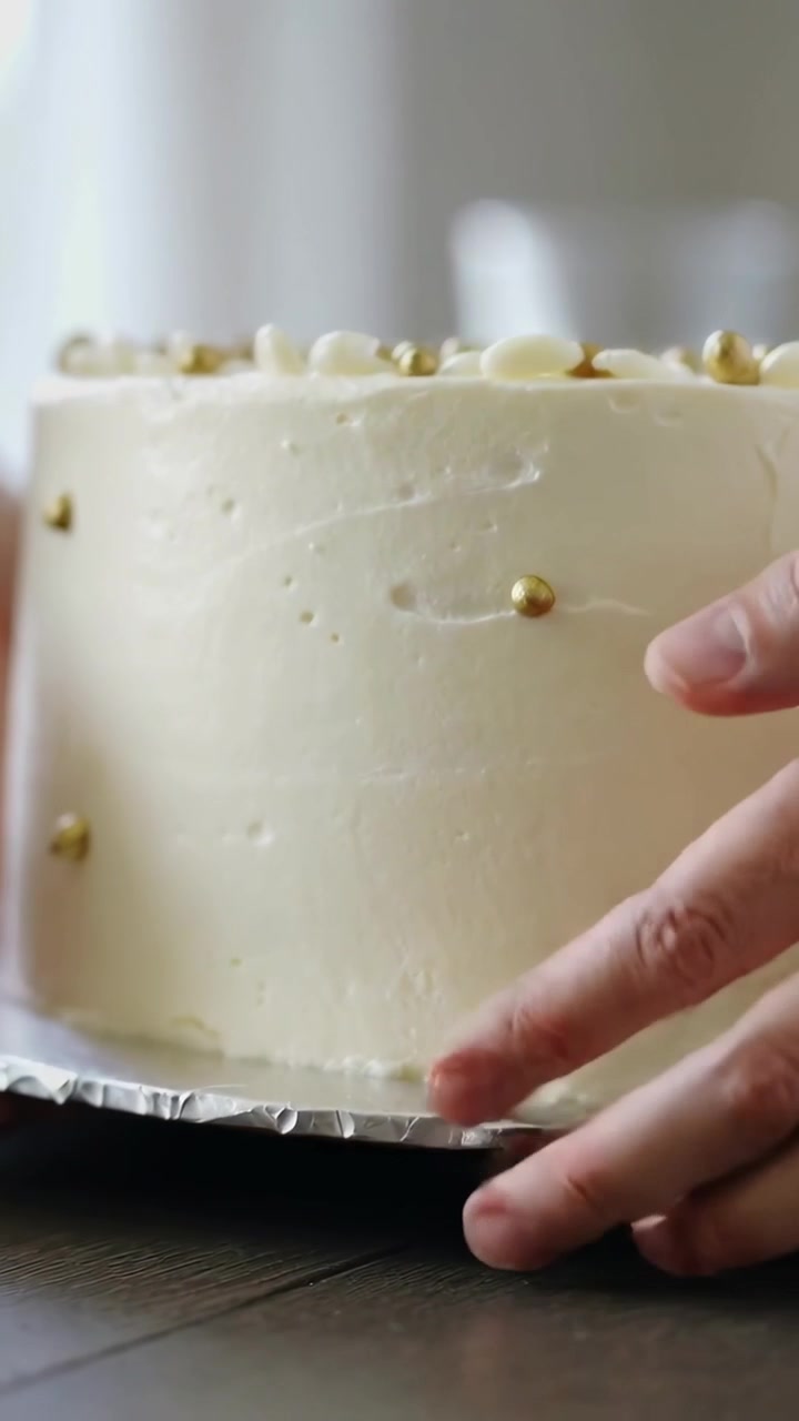 Video verticale: Sollevando una torta da un piedistallo, mani che la posizionano su un vassoio di cartone rivestito, allineandola su un tavolo per servire.