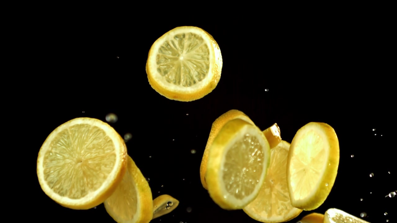 Fette di limone fresco che cadono al rallentatore con gocce d'acqua