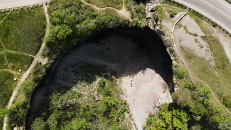 Descending-aerial-top-down-shot-of-gigantic-hole-with-ribbon-waterfall-on-Niagara-Escarpment,-in-the-Stoney-Creek-community-of-Hamilton,-Ontario,-Canada