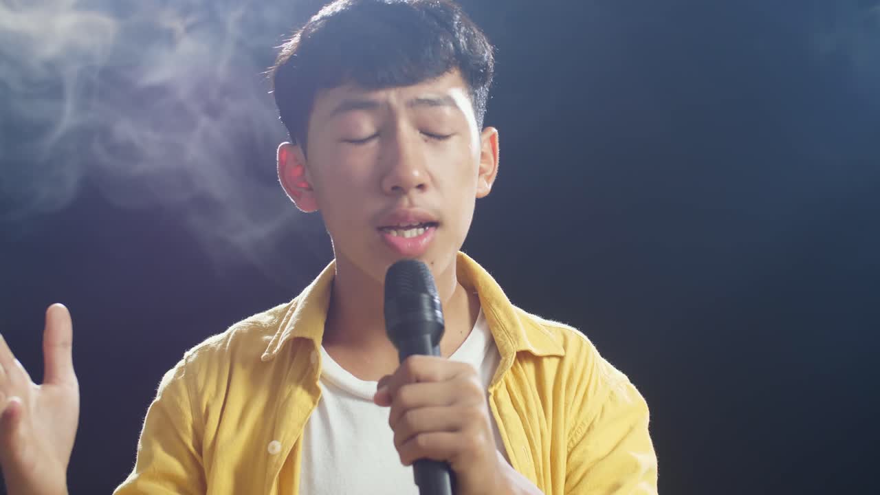젊은 아시아 소년이 마이크를 들고  연기 검은 배경에서 노래하는 클로즈업