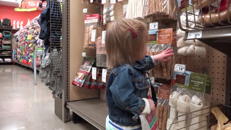 toddler in jean jacket shopping dog rawhide treats at pet store.